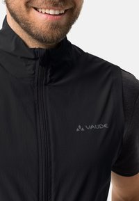 Schwarze ärmellose Jacke mit hohem Kragen, glatter Textur und Vorderreißverschluss. VAUDE-Logo in Grau auf der Brust.