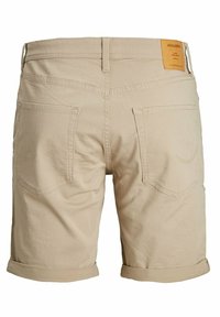 Pantalones cortos de algodón beige con dobladillos enrollados, dos bolsillos traseros y una etiqueta marrón en la cintura. Diseño de corte recto con costuras visibles.