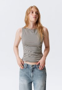 Top em riscas em bege e castanho escuro, com um design ajustado e mangas sem. Combinado com jeans de ganga em azul claro, desgastados.