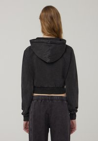 Felpa nera corta con cappuccio, dotata di maniche lunghe e orlo a costine. Il tessuto appare morbido con una sottile texture.