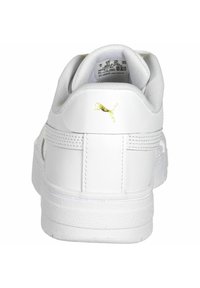Zapatilla blanca de cuero con un cuello acolchado, suela texturada y un pequeño logo dorado de Puma en el talón. Diseño simple y minimalista.