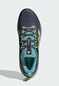 Scarpa sportiva blu scuro con tomaia in rete, dettagli turchesi e strisce riflettenti verde lime. Presenta un collare imbottito e lacci testurizzati.