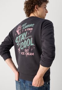 Σκούρος γκρι φούτερ με μακριά μανίκια, διακοσμημένο με πολύχρωμα γραφικά και κείμενο με θέμα το παγωτό στην πλάτη. Ραμμένες μανσέτες και ζώνη.