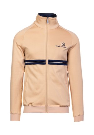 Beige zip-op jakke med høj krave, marineblå striber hen over brystet og logo på venstre side. Blødt materiale med ribstrikkede manchetter og kant.