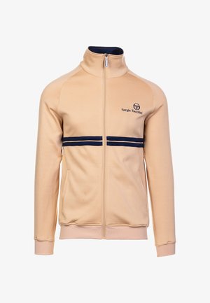 Bež zip-up jakk, millel on kõrge kaelus, tumedat sinist triipu rinna kohal ja logo vasakul küljel. Pehme materjal koos ribakraega varrukate ja äärtega.