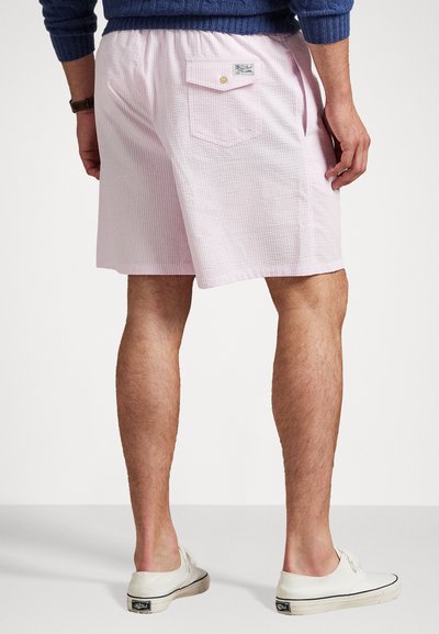 Šviesiai rožiniai, tekstūruoti šortai su užpakaline kišene ir etikete, dėvimi su baltais sportbačiais. Savybė - elastinga juostos juosta patogumui.