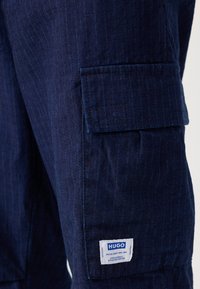 Navy blue cargo pants made of textured fabric with vertical stripes; features a side pocket and a HUGO brand label.