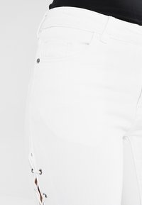 Jeans de denim blanco con un diseño ajustado, que cuentan con un detalle de cordones en el lateral y bolsillos estándar. Textura suave y acabado limpio.