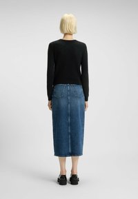 Svart stickad tröja och blå denim midi kjol. Tröjan har en figurnära design, rund halsringning och ribbade ärmslut. Kjolen har fickor bak.