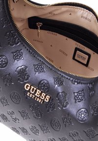 Borsa a tracolla in finta pelle nera con motivi floreali in rilievo e hardware in tono oro. La chiusura con zip rivela un interno beige con fodera stampata con logo.