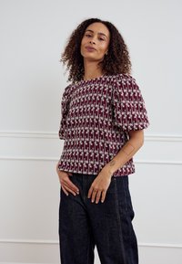 Burgundiapunane pihikuga pluus valge lillemustriga, ümar kaelus, tekstureeritud kangas. Kombineeritud tumeda teksariidest laiade pükstega.