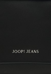 Czarna torba z fakturowanej skóry ekologicznej z srebnym logo "JOOP! JEANS". Gładkie akcenty i smukły design podkreślają jej nowoczesny charakter.