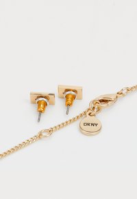 Orecchini a stud quadrati di colore oro con accenti arancioni e una catena che presenta un ciondolo circolare inciso con "DK NY". Design minimalista.