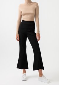 Krémový žebrovaný rolák a černé rozšířené kalhoty, doplněné bílými botami. Hladká textura a přiléhavý střih.