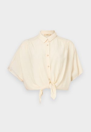 Gekürztes Hemd mit Knopfleiste in hellem Beige und Knoten vorne. Verfügt über kurze Ärmel und eine strukturierte Stoffqualität für mehr Tiefe.