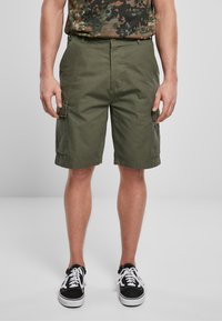 Pantaloni cargo color verde oliva, realizzati in cotone, con tasche laterali, una vestibilità comoda e orli arrotolati. Indossati con sneakers nere.