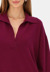 Bordowy sweter z dzianiny z kołnierzem, z dekoltem w serek i luźnym krojem. Miękka faktura z delikatnym połyskiem i widocznymi szwami.