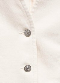Tissu couleur crème avec une texture côtelée subtile, comportant deux boutons-pression en métal argenté le long de la patte de boutonnage pour la fermeture.