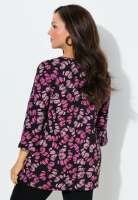 Schwarze Tunika mit einem rosa Blumenmuster und Schmetterlingsformen. Weicher Stoff, Rundhalsausschnitt, Dreiviertelärmel, leicht lockere Passform.