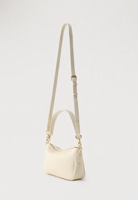 Kleine crèmekleurige leren schoudertas met verstelbare riem en gouden accenten, rechtop geplaatst op een eenvoudige lichte achtergrond.