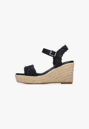 Sandalias de cuña negras con un diseño trenzado en la parte superior, correa ajustable en el tobillo y una suela plataforma de yute texturizado.