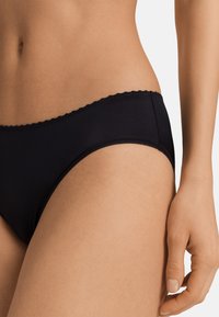 Pantaloni hipster neri in cotone con bordo in pizzo ondulato, caratterizzati da una texture liscia e un design aderente, che abbraccia comodamente la vita e i fianchi.