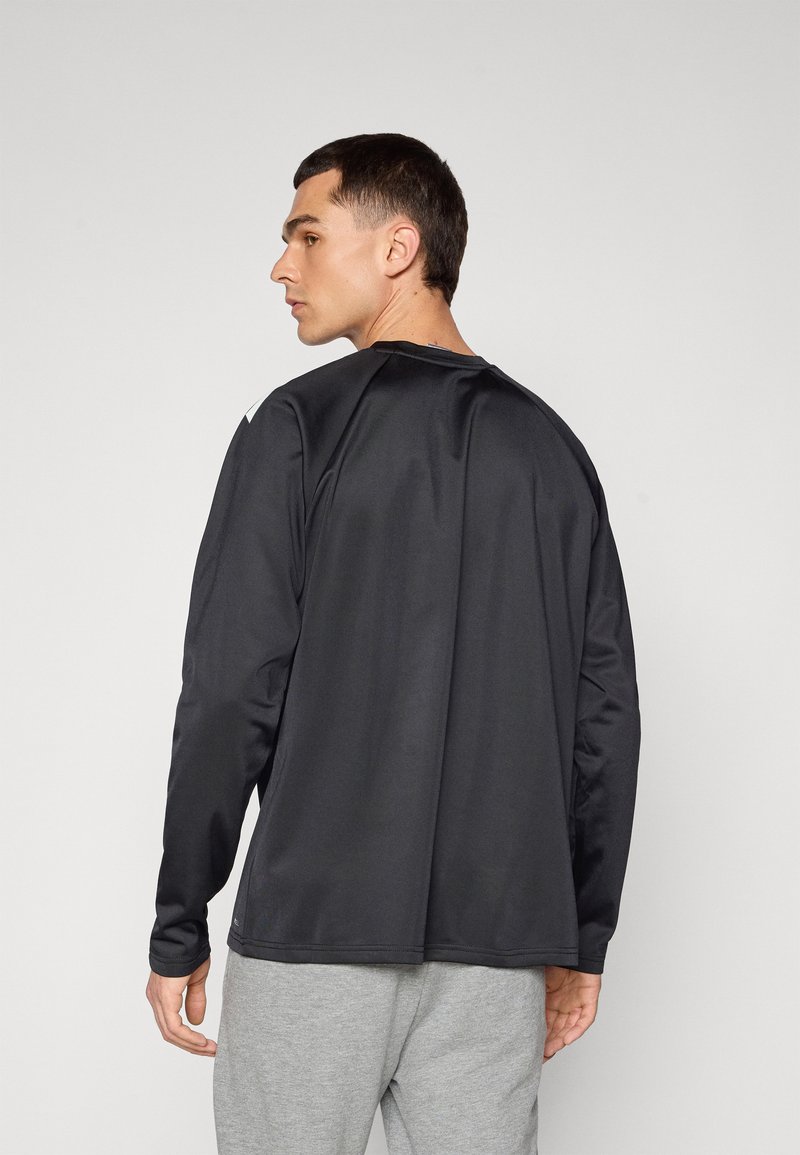 Zwarte lange mouwen shirt met een gladde textuur en ronde halslijn, heeft subtiele stikdetails en wordt gecombineerd met grijze broek.