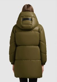 Groene pufferjas met een grote, gestructureerde capuchon. Voorzien van een zwarte logopatch, gestructureerde panelen en elastische manchetten. Gladde, glanzende afwerking.