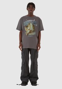 Grå oversized t-shirt med grafisk print af duer, parret med sorte cargo bukser med flere lommer og justerbare nederste kanter.