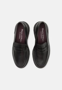 Mocassins en cuir noir au design classique, bout arrondi, empeigne rembourrée et détails de coutures visibles. Finition douce et texturée.