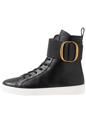 Czarny sneaker za kostkę z czarnymi sznurowadłami, szerokim paskiem i dużą złotą owalną klamrą, białą podeszwą oraz pętelką z tyłu.