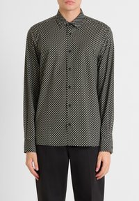 Camicia a maniche lunghe di colore verde scuro con un motivo geometrico in crema e nero. Presenta un colletto a punta e una chiusura con bottoni. Tessuto testurizzato.