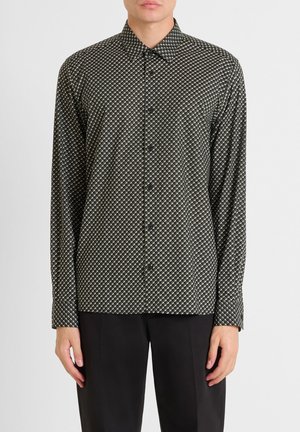Camisa de manga larga en verde oscuro con un patrón geométrico en crema y negro. Presenta un cuello puntiagudo y un cierre de botones en la parte delantera. Tejido texturizado.