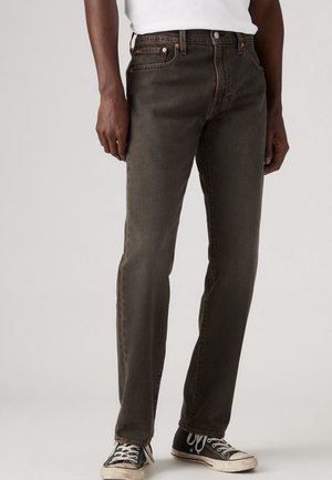 Mand iført mørkegrå straight-leg jeans og sorte high-top sneakers, stående mod en ensfarvet lys baggrund.