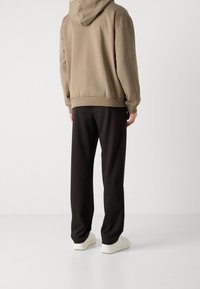 Brązowa bluza z kapturem i kieszenią kangurka, połączona z czarnymi spodniami dresowymi, oba wykonane z miękkiego materiału; dopełnieniem stroju są białe sneakersy.