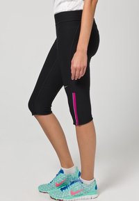 Černé capri legíny s přiléhavým střihem, s růžovým proužkem po straně a vysokým pasem. Nosené s vícbarevnými sportovními botami.