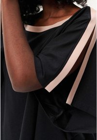 Haut noir à manches courtes avec un bord contrastant rose le long de l'encolure et des manches. Tissu lisse avec une coupe décontractée.