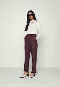 Top de manga longa branco com detalhes em renda, combinado com calças burgundy estampadas. Usado com óculos de sol pretos e sapatos de salto bloco bege.