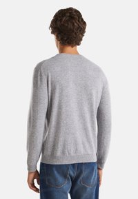Grå stickad tröja med rund halsringning och långa ärmar. Tyget verkar mjukt och strukturerat. Modellen vänder ryggen mot kameran, iförd blå jeans.