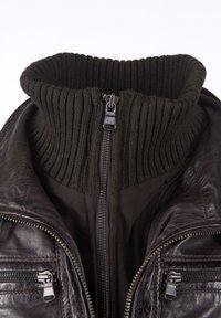 Ciemnobrązowa skórzana kurtka z zewnętrznym zamkiem błyskawicznym i wewnętrznym, grubym, prążkowanym kołnierzem, zapięta.