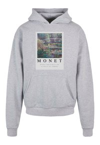 Szürke kapucnis pulóver, amely elöl egy Monet festményt ábrázol, rajta egy híddal, zöld környezetben, és a kép alatt szöveg található.