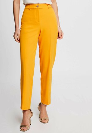 Pantaloni su misura giallo brillante con vita alta, dotati di un bottone decorativo, tessuto liscio e gambe affusolate. Abbinati a décolleté color nudo.