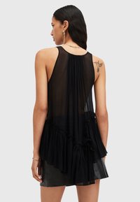 Black sleeveless top with layered ruffles, made from sheer fabric. Features a pleated back, tying accents, and a loose silhouette.