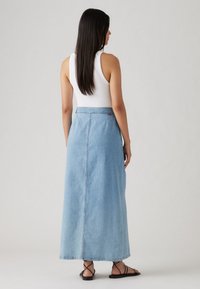 Lyseblå denim maxi nederdel med sidelommer og lige silhuet, båret med en hvid ærmeløs top og sorte sandaler.