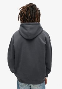Sudadera gris oscuro con un corte relajado, puños acanalados y una gran capucha. La tela parece tener textura y ser suave, adecuada para el uso casual.