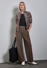  Leopard-print bomberjakke, sort top, brune brede bukser, hvide sneakers og en sort tote bag. Blødt stof, afslappet pasform.