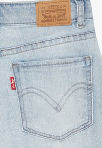 Jeans de mezclilla azul claro con un parche de cuero de marca en la cintura y un bolsillo trasero distintivo que presenta una etiqueta de logo roja y costura curvada.