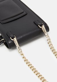 Borsa nera in ecopelle con tasca frontale, tracolla a catena dorata e dettagli in metallo. Texture liscia con design strutturato.