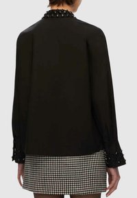 Blusa nera con maniche lunghe, collo e polsini decorati, con una texture liscia. Abbinata a una gonna a quadri.