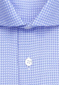 Chemise bleu clair à petits carreaux pied-de-poule, avec col visible et devant boutonné, boutons blancs.